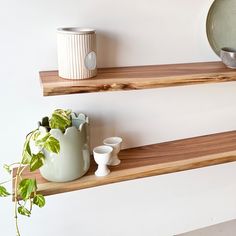 two wooden shelves with vases and plates on them next to a potted plant