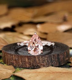 a pink diamond ring sitting on top of a piece of wood with leaves around it