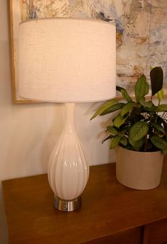 a white lamp sitting on top of a wooden table next to a potted plant