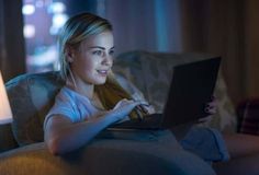 a woman sitting on a couch with a laptop computer in her lap looking at the screen