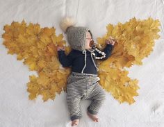 a baby wearing a knitted hat laying on top of a blanket covered in yellow leaves