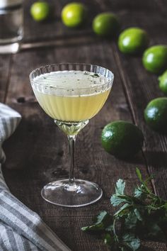 a margarita sitting on top of a wooden table next to limes