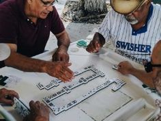 three men sitting at a table working on some type of project with other people around them