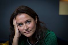 a woman sitting down with her hand on her head and looking at the camera while wearing a green sweater