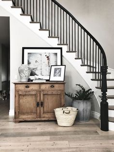 an entryway with stairs and pictures on the wall next to a cabinet in front of it