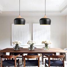 a dining room table with four chairs and two vases filled with flowers on it