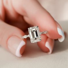 a woman's hand holding an engagement ring with a large emerald stone in it