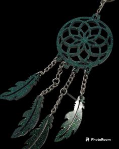 a green dream catcher with feathers hanging from it's side on a black background