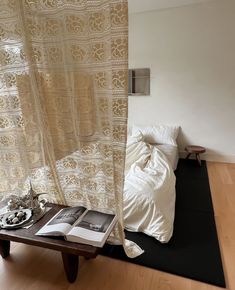 an open book sitting on top of a wooden table next to a window with sheer curtains