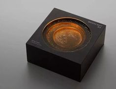 a small black box with a gold colored object in it's center on a gray surface