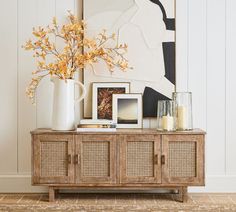 a white vase with yellow flowers on top of a wooden cabinet next to pictures and candles