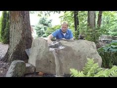 a man sitting on top of a large rock next to a forest filled with trees