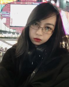 a woman wearing glasses and a black jacket in front of a neon sign at night