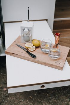 a cutting board topped with lemons and two glasses on top of a white table