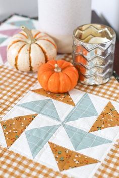 a quilted table runner with two pumpkins on it and a candle holder in the background