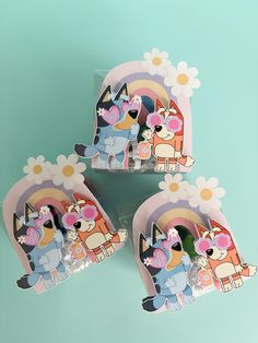 three pieces of paper with cartoon characters on them and flowers in the middle, sitting on a blue surface