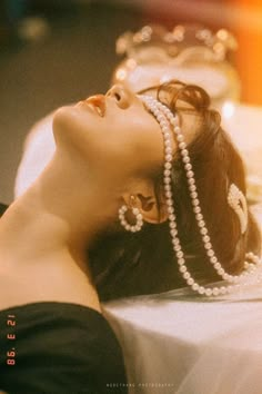 a woman laying down with pearls on her head