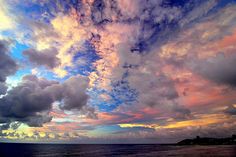 the sky is filled with colorful clouds as the sun sets over the ocean and land