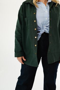 a woman standing in front of a white wall wearing a green jacket and blue striped shirt