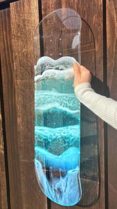 a person is holding up a glass vase with blue liquid in it on a wooden fence