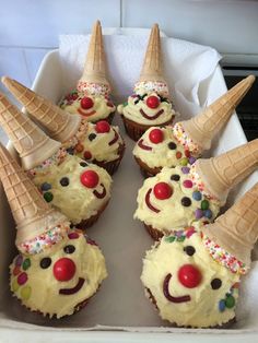 cupcakes decorated with ice cream and clown faces are in a white box on the counter