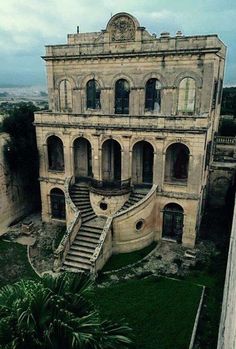 an old building with stairs leading up to the top floor and green grass in front of it