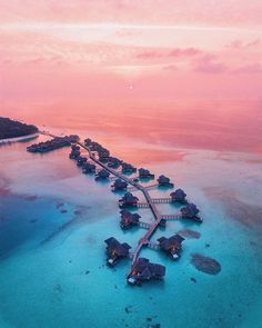 an aerial view of the ocean with over water huts and walkways leading to them