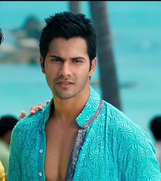 two men standing next to each other in front of the ocean with palm trees behind them