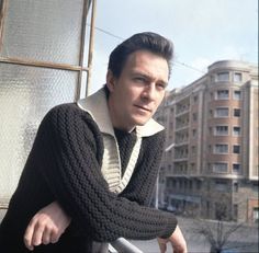 a man leaning on a rail in front of some buildings