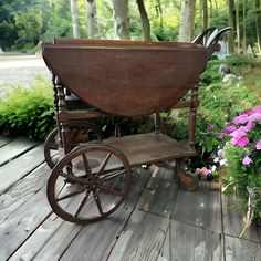 an old wooden wagon sitting on top of a wooden deck next to flowers and trees