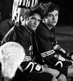 two young men sitting next to each other on top of a tennis racquet