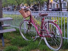 a red bicycle parked next to a wooden bench in front of a white picket fence