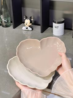 a person holding a heart shaped dish in front of a mickey mouse figurine