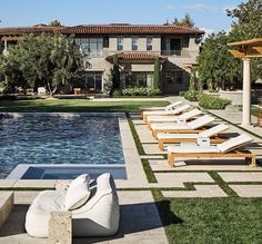 an outdoor swimming pool with lounge chairs next to it and a house in the background