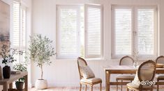 a dining room with white walls and wooden flooring, windows covered in shutters