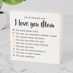 a wooden sign with the words i love you mom written on it next to a potted plant