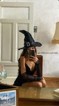 a woman dressed as a witch taking a selfie with her cell phone while sitting on the floor