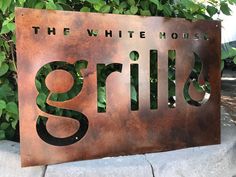 a metal sign that says the white house grills on it's side in front of some bushes