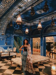 a woman standing in an ornately decorated room with blue walls and chandeliers