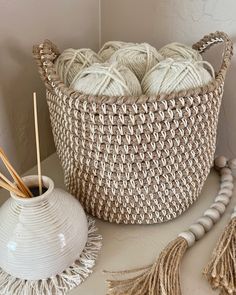 a basket filled with balls of yarn next to a white vase and bead tassels