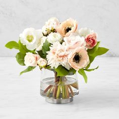 an arrangement of flowers in a glass vase on a marble table with white and grey background