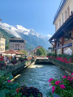 a river running through a lush green hillside covered in flowers and surrounded by tall buildings