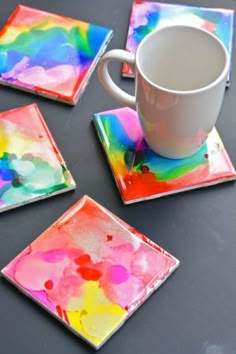 four square coasters with colorful paint on them and a coffee cup in the middle