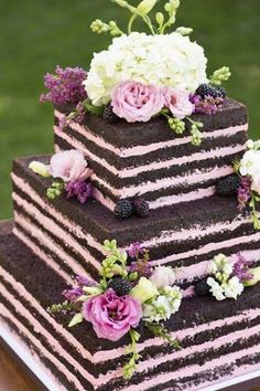 a triple layer cake with flowers and berries on top is sitting on a wooden table