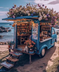 an old blue truck parked on the beach with bookshelves and flowers in it