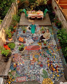 two people sitting on a bench in the middle of a small garden with lots of potted plants