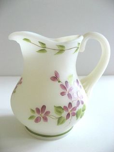 a white pitcher with purple flowers painted on the side and green trim around the bottom