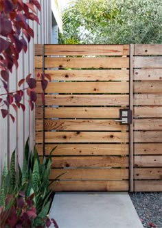 a wooden gate in the middle of a yard with gravel and plants on either side