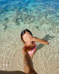 a woman standing on top of a sandy beach next to the ocean holding her hand up