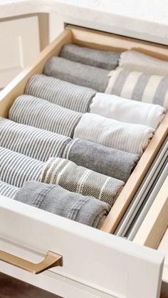 an open drawer filled with folded towels and striped linens on top of a wooden table